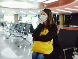 woman sitting at the airport with luggage in a medical mask waiting for a flight photo