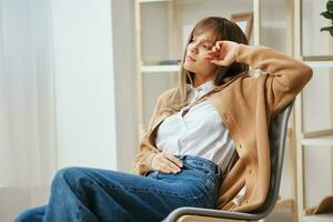 Thoughtful pensive young blonde lady in warm sweater dreams about future holidays sitting in armchair at home interior. Pause from work, take a break, reflections in free time concept. Copy space photo