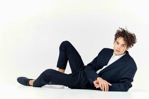 a man with curly hair lies in a suit on the floor in a bright room and sneakers style photo