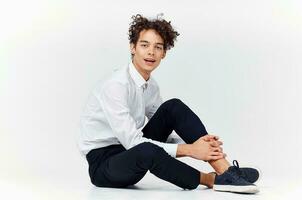 a teenager in a suit and sneakers sits on the floor In a bright room side view photo