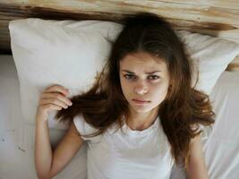 a woman lies in bed in a white t-shirt feeling unwell close-up photo