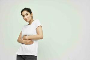 brunette in white t-shirt holding her belly menstruation health problems dissatisfaction photo