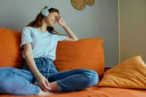 pretty woman listening to music with headphones on the orange sofa unaltered photo