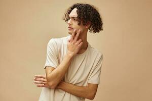 Unhappy discontented awesome tanned curly man in basic t-shirt with disgust looks aside posing isolated on beige background. Fashion New Collection offer. People Emotions concept. Free place for ad photo