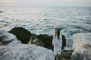 Woman in white dress with wet hair on the ocean stones photo