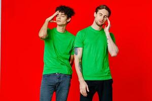 two friends in green t-shirts are standing next to tin with their hands emotions red background photo