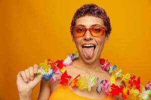 retrato de un mujer con un floral hawaiano guirnalda alrededor su cuello es teniendo divertido bailando y sonriente en brillante ropa en un naranja antecedentes vistiendo Gafas de sol, estilo de vida fiesta hawaiano estilo foto