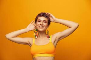 Portrait of a young woman with a short haircut and colored hair smiling and showing her tongue at the camera on an orange background with earrings accessories in the studio photo