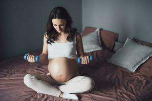 Pregnant woman is exercising with weights at home. photo