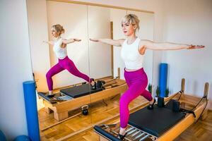 Blonde woman is exercising on pilates reformer bed in her home. photo