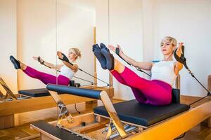 Blonde woman is exercising on pilates reformer bed in her home. photo