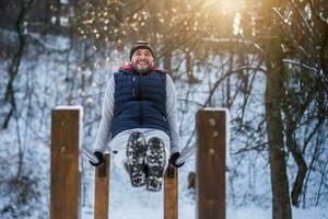 Adult man is exercising on push-up bar in park in wintertime. photo