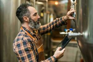 Man is working at craft beer factory. He is operating machinery in brewery. Small family business, production of craft beer. photo