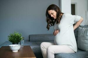 Pregnant woman with back pain at home. Hands in the back. photo