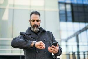 Businessman looking ah his watch in black clothing standing in front of company building photo