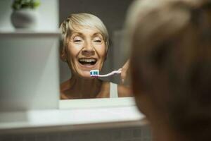 Beautiful mature woman is doing her dental hygiene in the bathroom photo