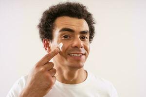 Multiracial man applying facial cream. Self care concept. photo