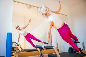 Blonde woman is exercising on pilates reformer bed in her home. photo