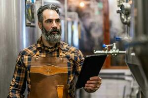 Man is working at craft beer factory. He is operating machinery in brewery. Small family business, production of craft beer. photo