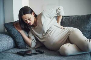 Pregnant woman with back pain at home. Hands in the back. photo