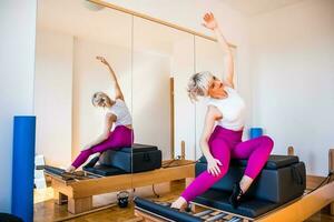 Blonde woman is exercising on pilates reformer bed in her home. photo