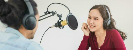 Smile two asian young woman, man radio hosts in headphones, microphone while talk, conversation, recording podcast in broadcasting at studio together. Technology of making record audio concept. photo