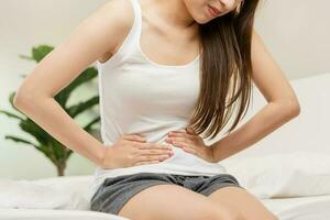 Flatulence asian young woman, girl hand in stomach ache, suffer from food poisoning, abdominal pain and colon problem, gastritis or diarrhoea. Patient belly, abdomen or inflammation, concept. photo