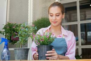 Smiling, happiness asian young woman, girl gardener holding, taking care flowers of pot plants, engaging hobby at home. Love gardening of plants and care. Owner small business concept. photo