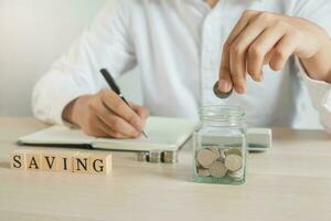 Close up hand of young asian businessman puts a coin into the jar to calculate and financial plans to spend enough money on his income for saving money. photo