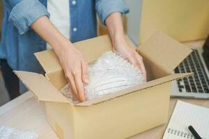 Small business entrepreneur SME, hand of woman owner packing product, checking parcel before into cardboard box after receive order from customer, working at home office. Merchant online, ecommerce. photo