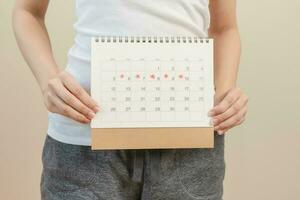 Menstruation, periods cycle day of monthly, hurt asian young woman, female hand holding, marking symbol on calendar for missed and delay or late. Medical, healthcare, gynecological concept. Copy space photo