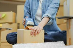 Small business entrepreneur SME, asian young woman,girl owner packing product, checking parcel for delivery to customer, using scotch tape to seal the box, working at home. Merchant online, e commerce photo