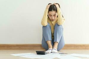 Financial owe asian woman, female sitting on floor home, stressed and confused by calculate expense from invoice or bill, have no money to pay, mortgage or loan. Debt, bankruptcy or bankrupt concept. photo
