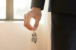 Home agent, broker man in suit standing, realtor holding the house key to hand over to new homeowner or tenant , client after the bank approved the home loan, mortgage loan. Property lease of landlord photo