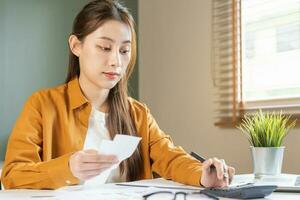 Asian young employee, business woman calculate tax income and expenses, bills, credit card for payment or payday on table at home office. Financial, finance people concept. photo