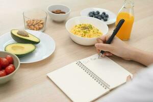 dieta, dieta mano de asiático joven mujer, niña escribir dieta plan nutrición en mesa es diferente comida ingredientes en el verde. nutricionista de saludable, nutrición de peso pérdida, salud cuidado gente. foto