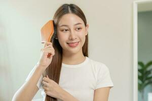 Health hair care, beauty makeup asian woman, girl holding hairbrush and brushing, combing her long straight hair looking at reflection in mirror in morning routine after salon treatment, hairstyle. photo