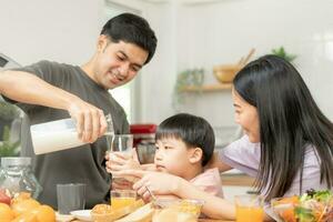 Happy refreshment family breakfast in morning, asian young parent father, mother and little cute boy, child having meal in kitchen eating together at home. Cheerful, enjoy cooking people. photo