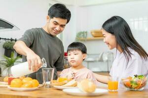 contento refresco familia desayuno en mañana, asiático joven padre padre, madre y pequeño linda chico, niño teniendo comida en cocina comiendo juntos a hogar. alegre, disfrutar Cocinando gente. foto