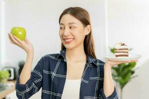 dieta asiático joven mujer perder peso para salud elegir a comer verde manzana, Fruta hacer no escoger comer chocolate pastel, panadería porque será hacer grasa cuando hambriento, hembra peso pérdida persona, tentación comida foto