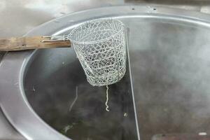 Strainer basket for blanching noodles laying over a pot covered with steam. photo