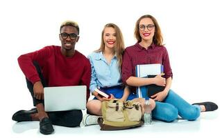 Three students sitting with books, laptop and bags isolated on white background photo