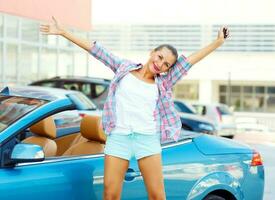 Young emotional woman standing near a convertible with the keys in her hand photo