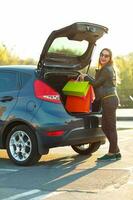 caucásico mujer poniendo su compras pantalones dentro el coche maletero foto