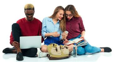 Three students sitting with books, laptop and bags isolated on white background photo