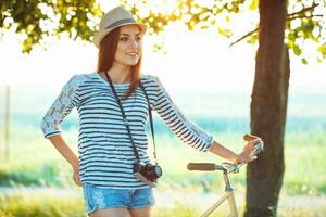 encantador joven mujer en un sombrero montando un bicicleta en un parque foto