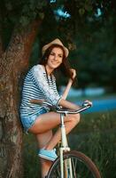 Lovely young woman in a hat with a bicycle in a park photo