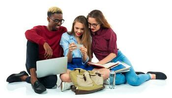 Three students sitting with books, laptop and bags isolated on white background photo