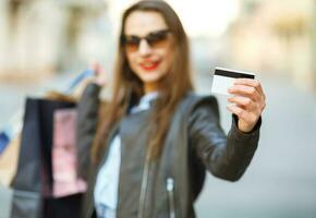 contento hermosa mujer con compras pantalones y crédito tarjeta en el manos en un calle foto