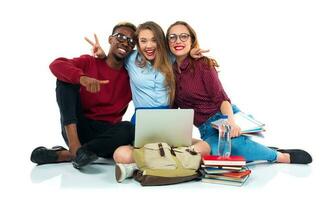 Three students sitting with books, laptop and bags isolated on white background photo